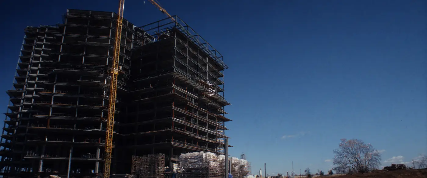 A mid-rise building under construction, its structural frame and tower crane against open sky.