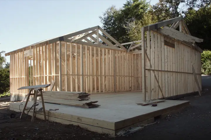 A timber-framed building under construction, with lumber stacked on the deck.