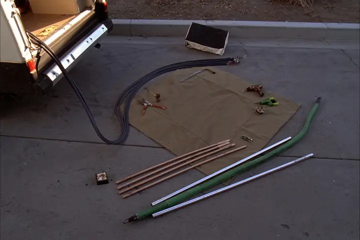 Copper pipe, cable and hand tools laid out beside a work van.